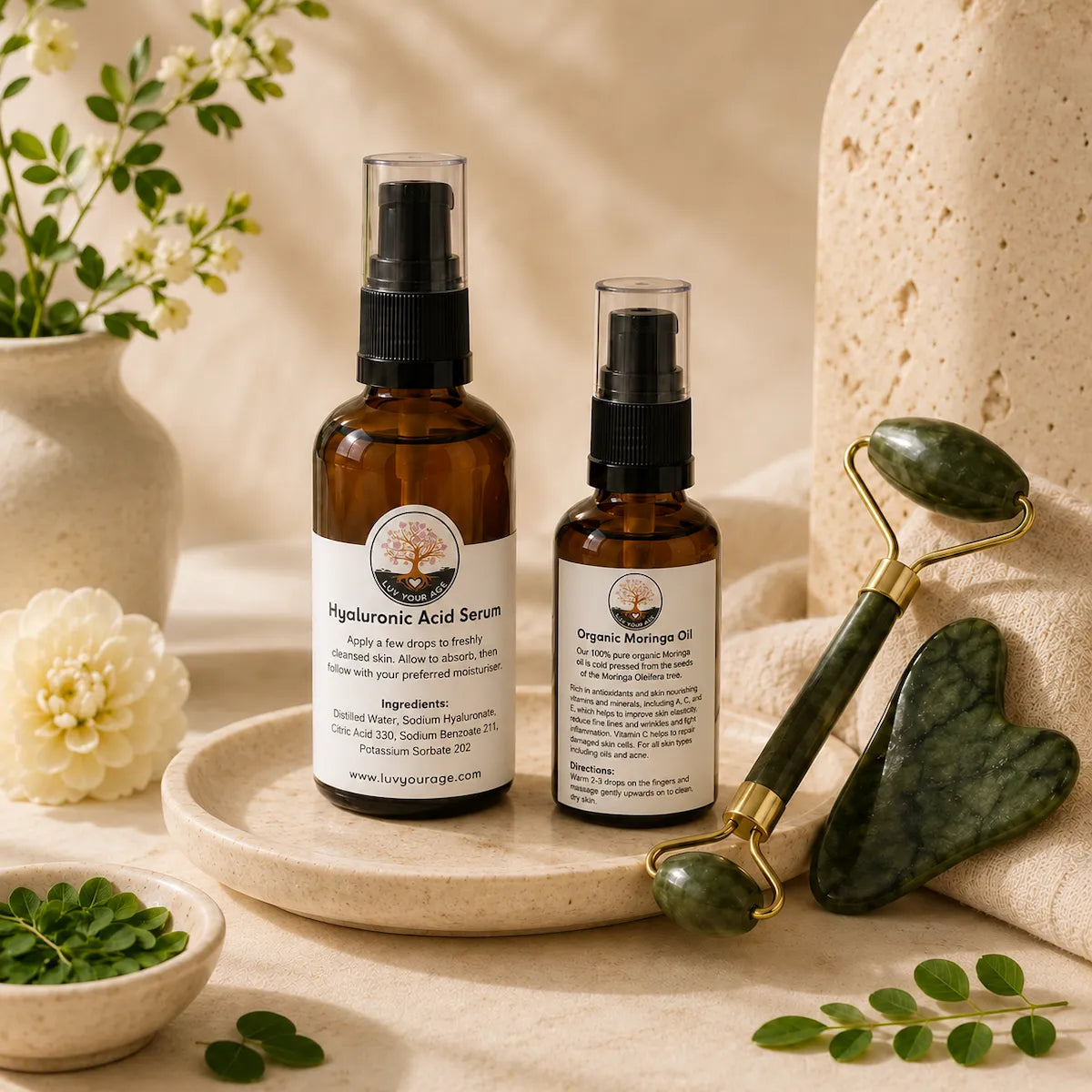 Luv Your Age Hyaluronic Acid Serum and Organic Moringa Oil with jade roller and gua sha on a neutral stone tray, styled with botanical accents and soft natural lighting for a premium skincare and wellness display.