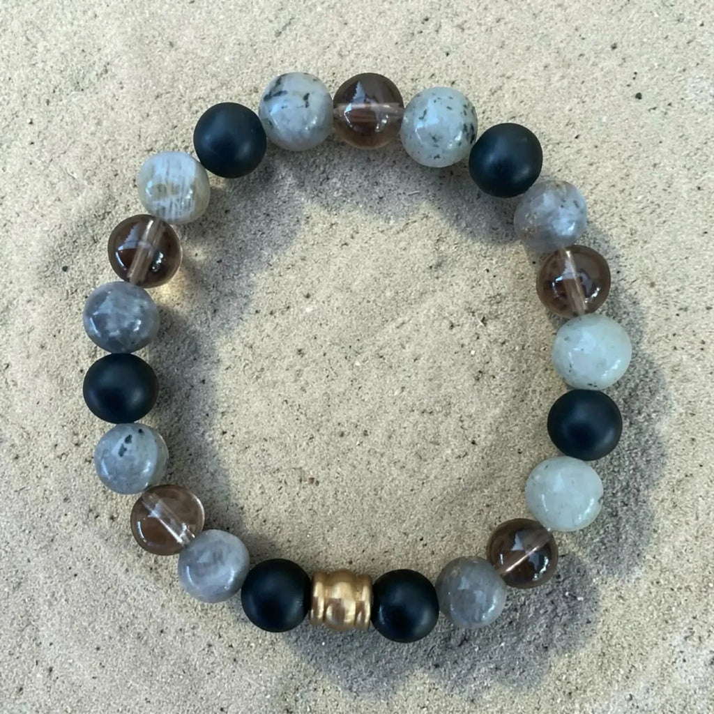 Grounded strength beaded bracelet with black, white, and gold charm on a beige surface.