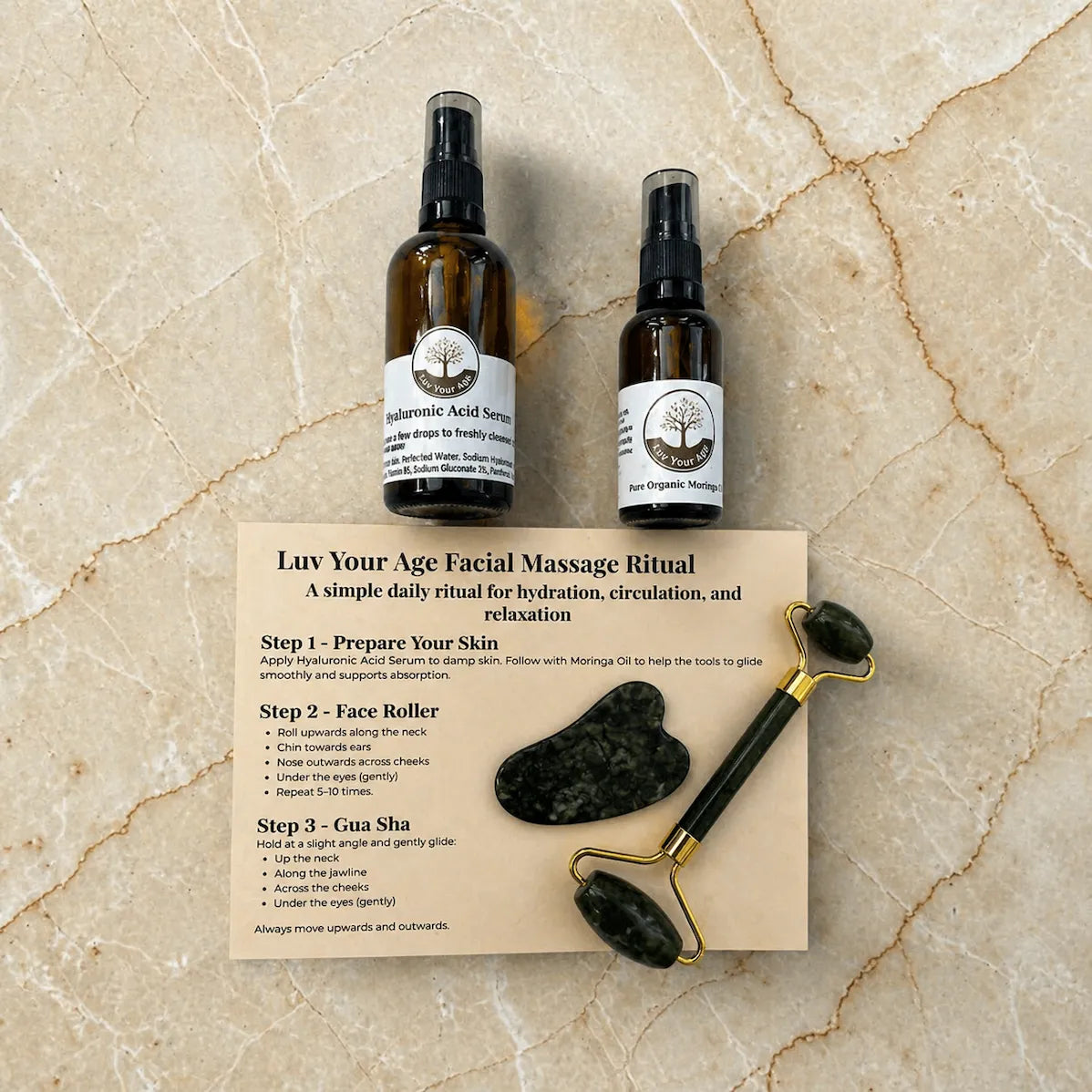 Two bottles of facial serum and moringa oil, a roller, and gua sha tools on a beige marble surface with a step-by-step guide.