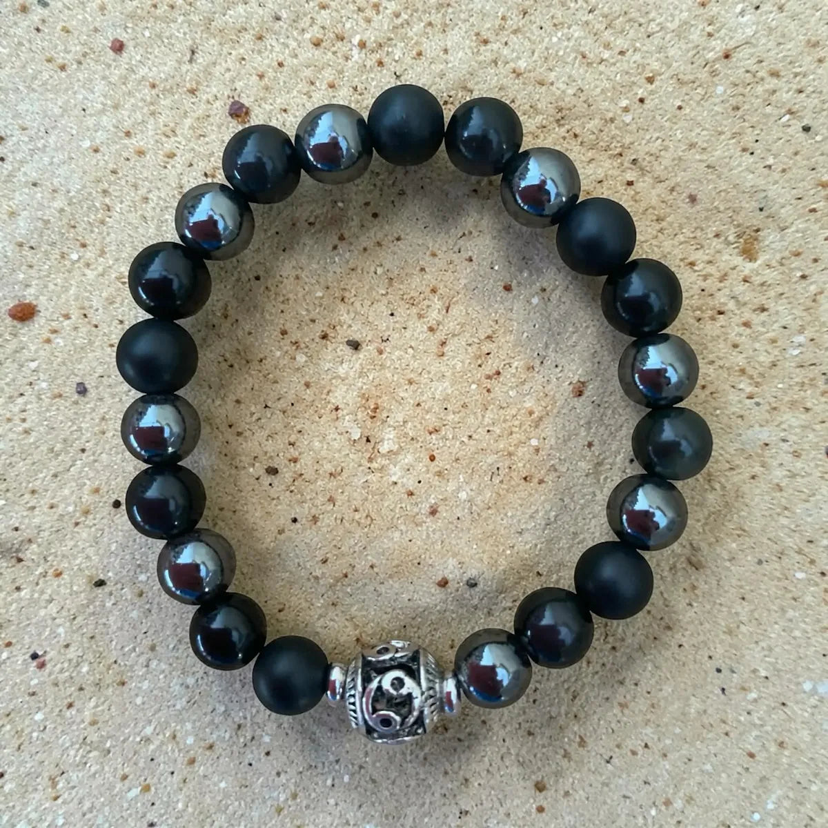 Black hero protection beaded bracelet with a silver charm on a beige surface.