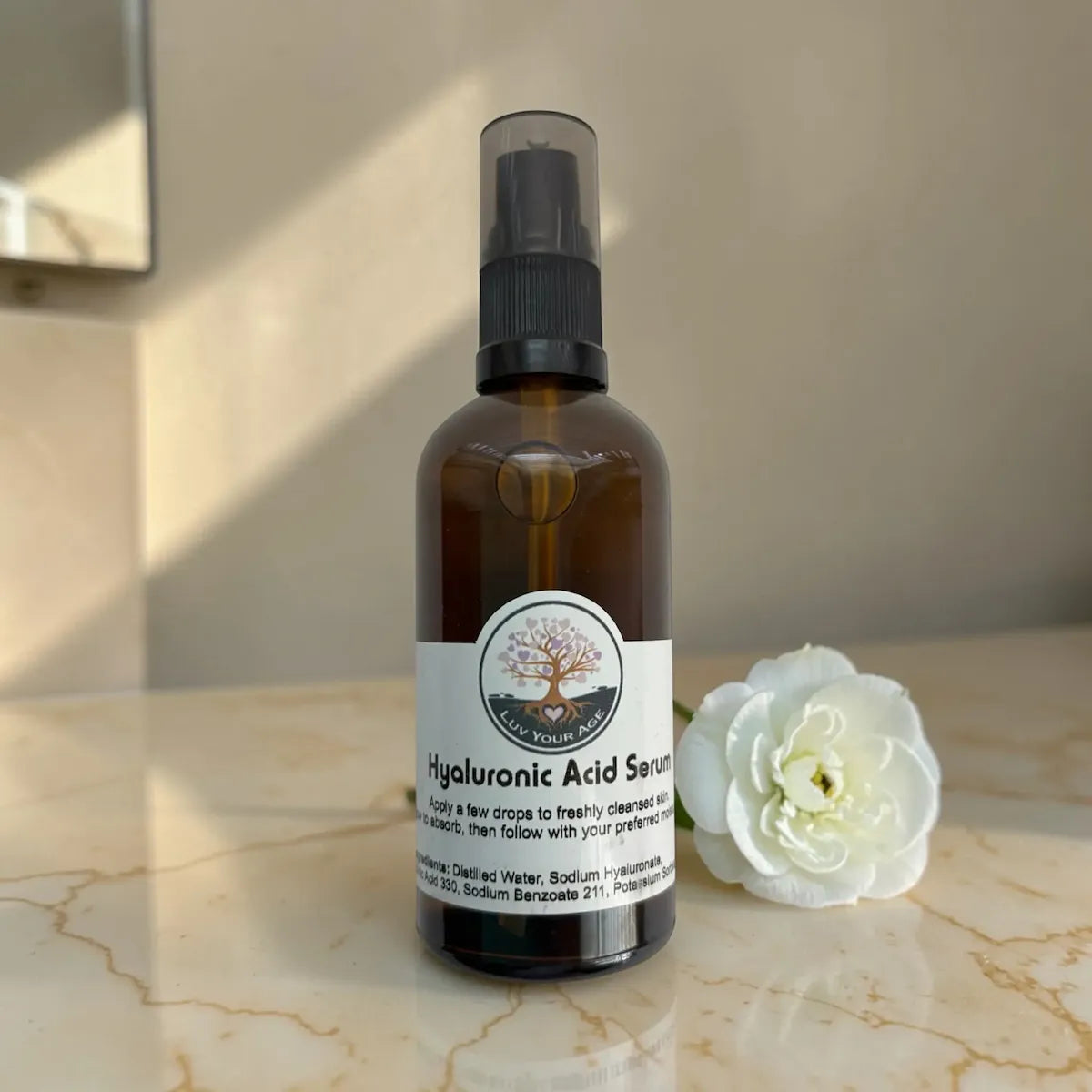 Brown serum bottle with black spray nozzle on a marble surface with a white flower.