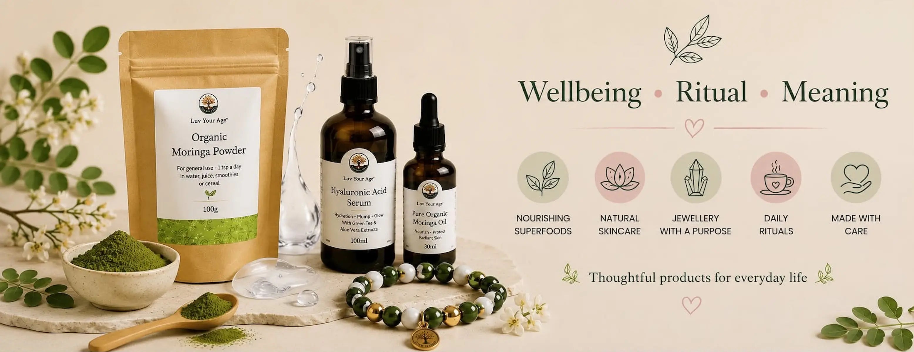 Luv Your Age product flatlay featuring Organic Moringa Powder, Hyaluronic Acid Serum, Pure Organic Moringa Oil, and a beaded bracelet, surrounded by moringa leaves and white flowers, with 
the tagline Wellbeing, Ritual, Meaning and icons for Nourishing Superfoods, Natural Skincare, Jewellery with a Purpose, Daily Rituals, and Made with Care.