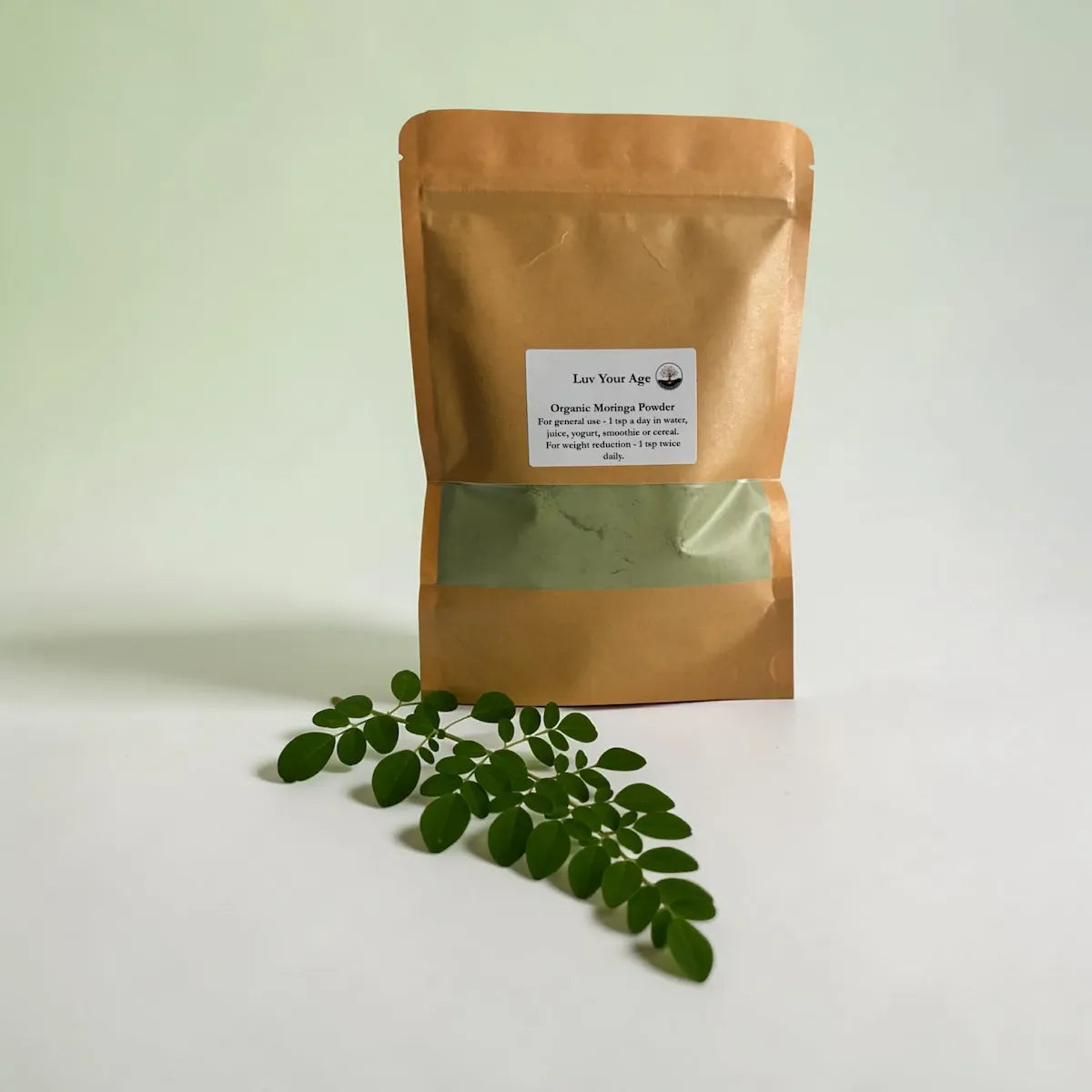 Brown packaging of organic moringa powder with moringa leaves on a light background.