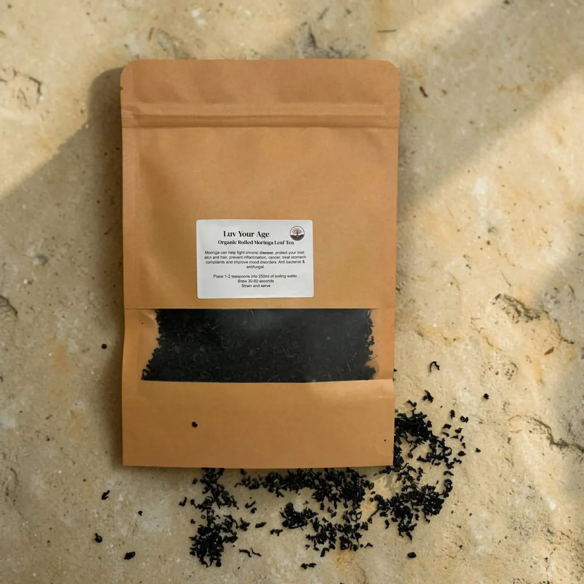 Brown paper bag with rolled moringa on a beige stone surface.
