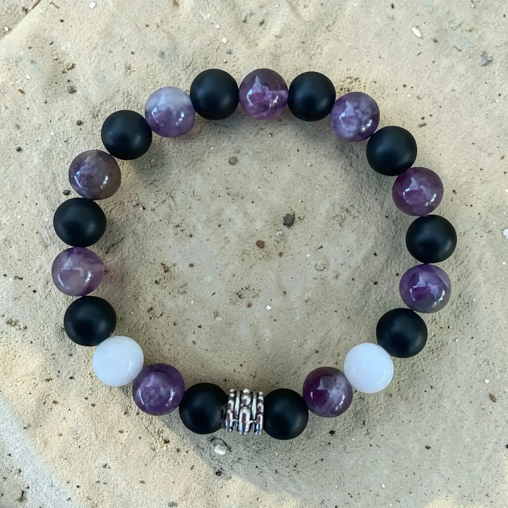 Beaded soft protection bracelet with black, purple, and white beads on a textured surface.