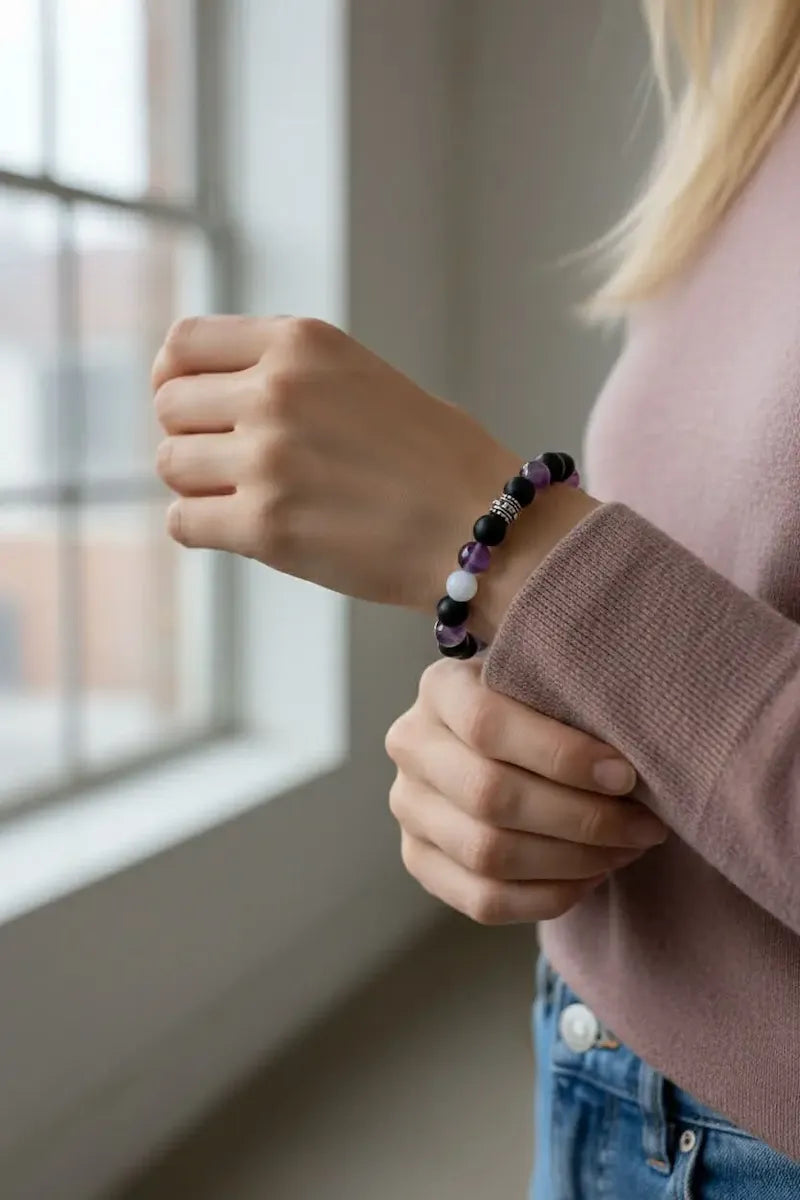 Person wearing a beaded soft protection bracelet with a blurred window background.