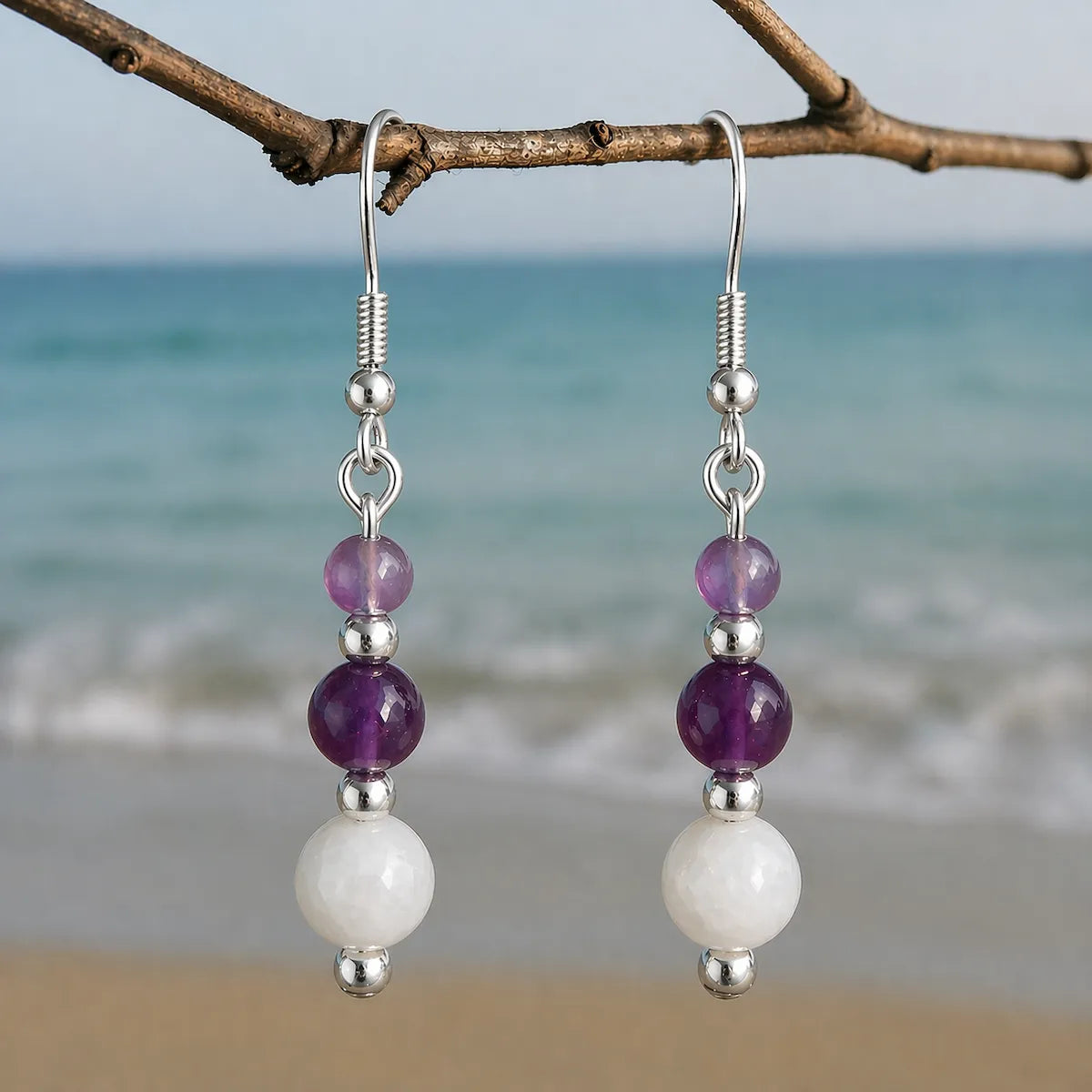 Soft Protection earrings with moonstone and amethyst gemstones on silver hook hanging on branch by the sea.